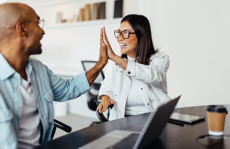Happy business people sitting at a table and giving each other a high five. Young business people celebrating success in an office.