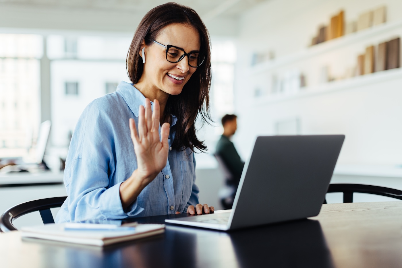 Woman waving on a video call while sitting in an office. Female designer having an online meeting with her business clients on a laptop.