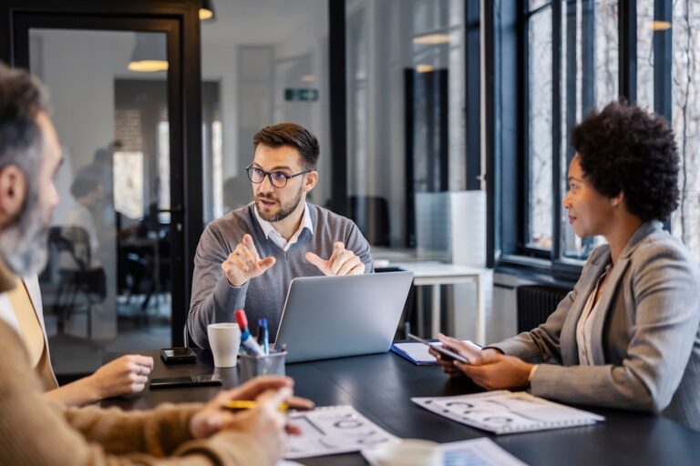 A manager is sitting at meeting room with his multicultural coworkers and collaborating on a project.