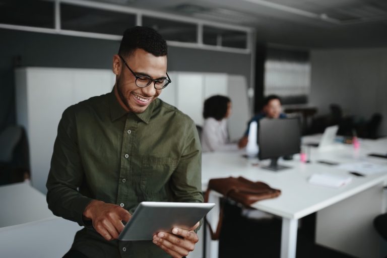 Successful smiling young man in office using digital tablet