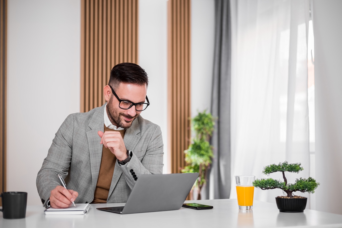 Delighted adult businessman, checking the company income on his laptop, writing it down.